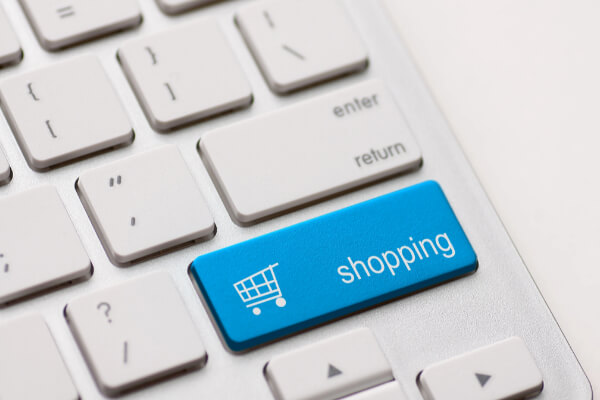 A close-up, high-angle shot of a white computer keyboard with a prominent, bright blue key with the word "shopping" and a shopping cart icon on it. The button is located near the "enter" and "return" keys.