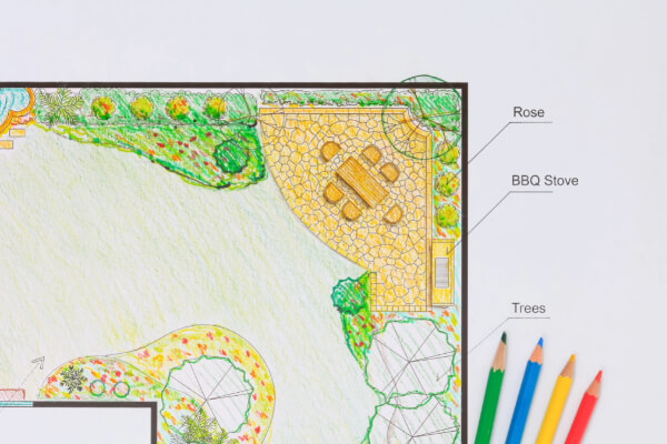 A detailed, hand-drawn landscape architecture blueprint and design plan of a residential backyard. The design includes a lawn, a patio with a table and chairs, a barbecue stove, and a variety of trees and plants, including a rose bush.