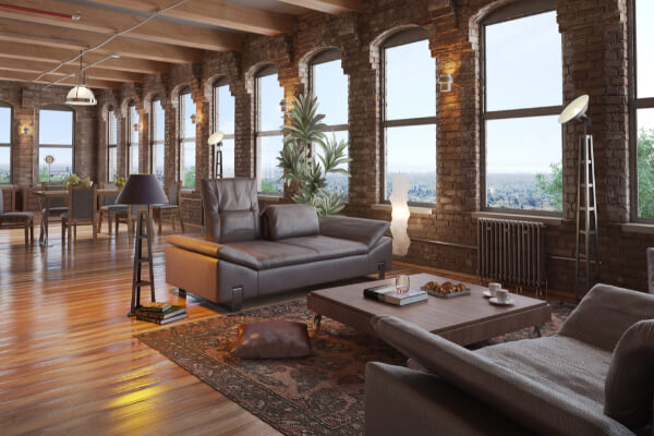 A wide-angle, hyper-realistic, and brightly lit image of a spacious, open-concept loft apartment with a mix of industrial and modern interior architecture. The living room has exposed brick walls, a dark leather sofa, hardwood floors, and large arched windows with a view of the city.