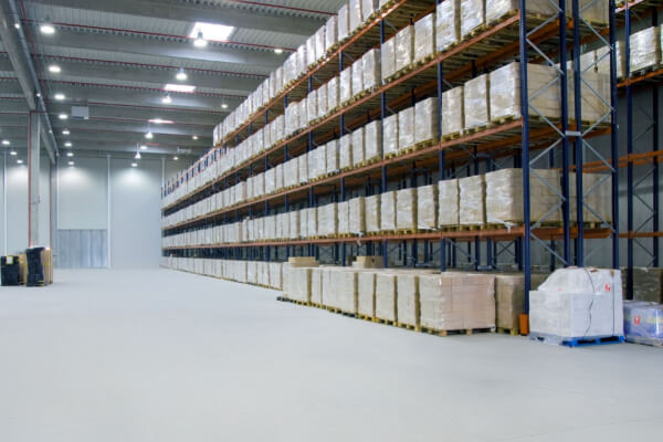 A wide-angle, hyper-realistic, and low-angle shot of tall warehouse racks filled with a variety of goods on wooden pallets. The shelves are packed with inventory, including shrink-wrapped boxes, with a dark and moody lighting effect.