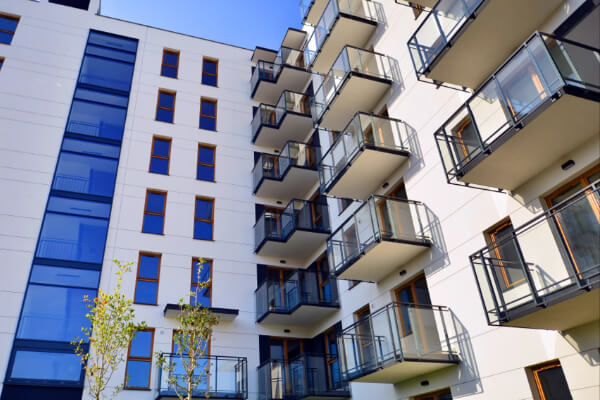 A modern residential condominium building with a white facade, featuring multiple floors of glass-paneled balconies. The clean lines and large windows reflect the clear blue sky, emphasizing the contemporary architectural style.