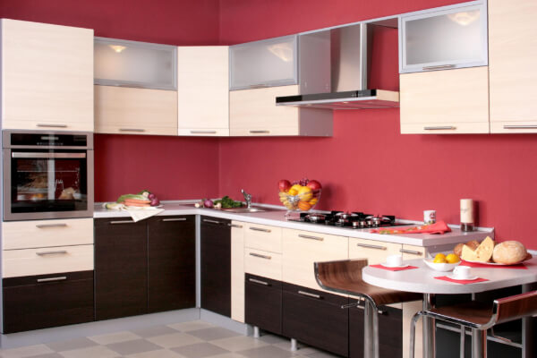 A vibrant, colorful, and modern kitchen interior featuring a bold red accent wall and two-toned cabinets—white upper cabinets and dark brown lower cabinets. The space also includes a stainless steel oven and range hood, a breakfast bar with two stools, and a black and white checkerboard floor.