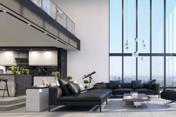 A modern, open-concept loft apartment with a minimalist interior design. The living room has a large black leather sofa, a glass coffee table, and an upstairs mezzanine with a steel railing. The living area also features floor-to-ceiling windows with a city view.