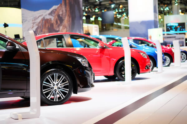 A side-view, low-angle shot of a row of colorful new vehicles—including brown, red, and blue cars, on a platform in an automotive show exhibition hall.