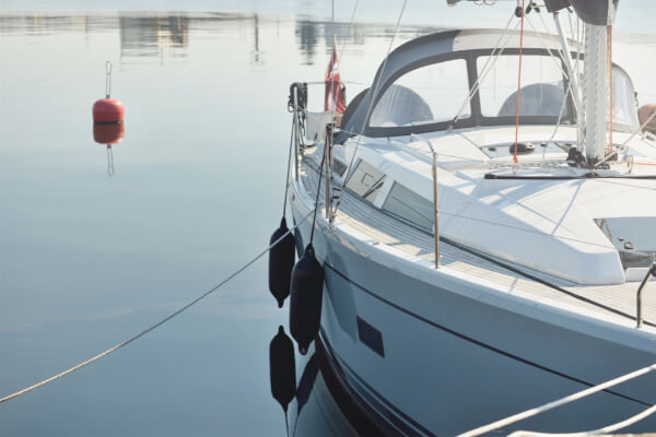 A side-view, eye-level shot of a clean sailboat with a small red flag, docked on a calm, serene lake. The water reflects the sky, and a red buoy floats nearby.