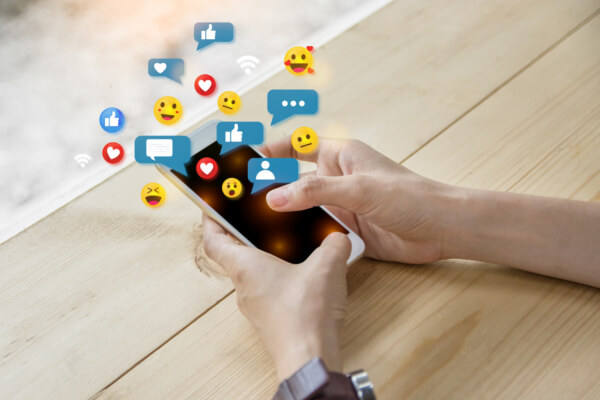 A person holding a smartphone with digital social media icons like likes, hearts, and speech bubbles floating above the screen for AI sentiment tracking.