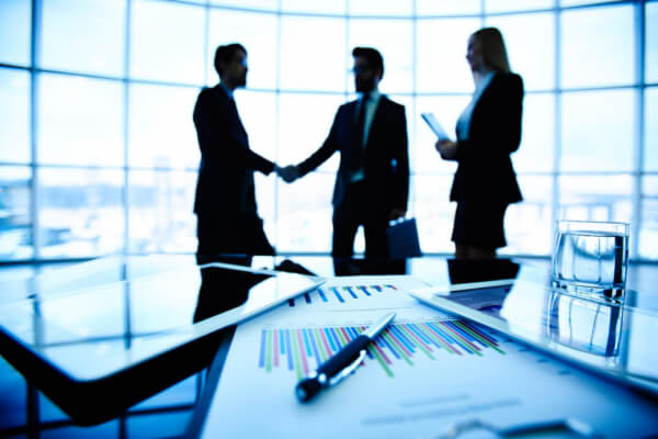 Silhouettes of business professionals shaking hands in a modern glass office, representing an AI-facilitated B2B sales partnership.