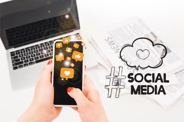 A smartphone displaying social media notification icons in front of a laptop and newspapers, symbolizing AI-integrated content marketing.
