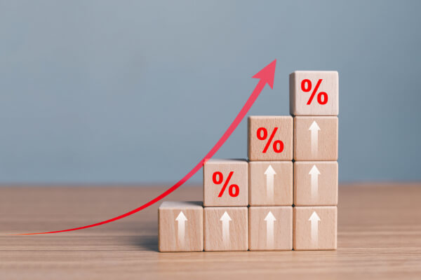 Wooden blocks stacked as a rising staircase with percentage symbols and a red upward arrow, representing scalable AI sales success.