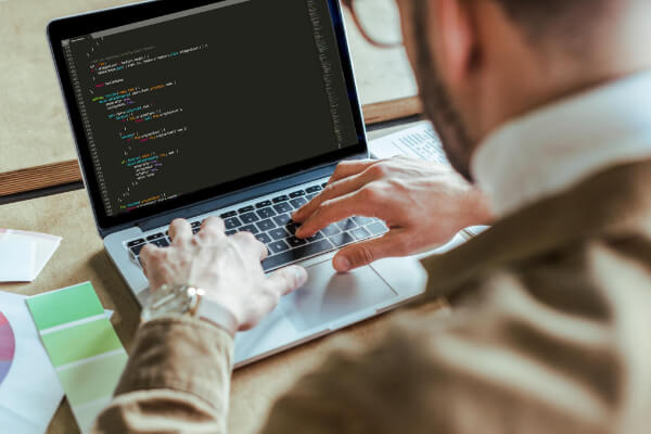 Over-the-shoulder view of a developer typing code on a laptop keyboard, with color swatches visible on the desk.