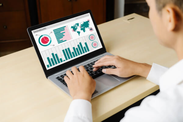 A person typing on a laptop displaying a custom business dashboard with a world map and bar charts.