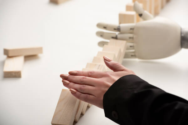 A woman's hand stopping a line of falling wooden dominoes right before they are pushed by a mechanical robot hand.