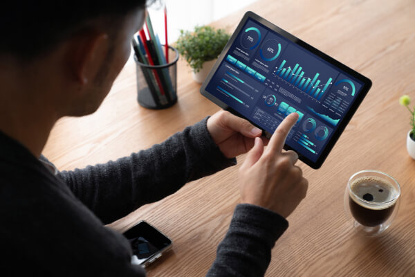 Over-the-shoulder view of a person using a tablet to interact with a dark-themed custom analytics dashboard.